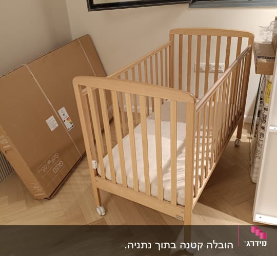 מיטת תינוק מעץ בחדר עם קרטון גדול ליד